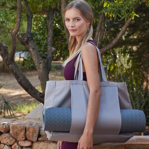 May include: A gray canvas tote bag with a yoga mat tucked inside. The bag has two handles and a zipper closure. The yoga mat is blue and has a geometric pattern.