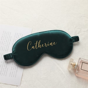 以下が含まれることがあります： 「Catherine」という名前が金色の文字で刺繍された、濃い緑色のサテン製のアイマスクです。