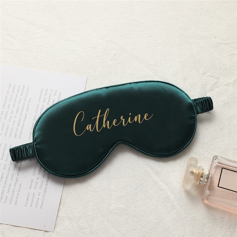 以下が含まれることがあります： 「Catherine」という名前が金色の文字で刺繍された、濃い緑色のサテン製のアイマスクです。