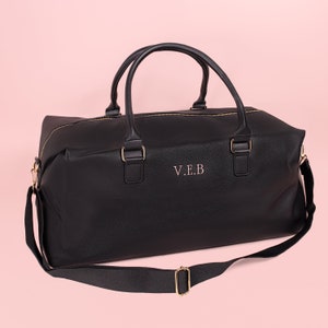 May include: Black leather duffel bag with a gold zipper and a gold strap. The bag has a personalized inscription that reads "V.E.B."