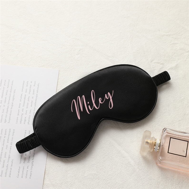 以下が含まれることがあります： ピンクの文字で「Miley」と刺繍された、黒いサテン製のアイマスクです。