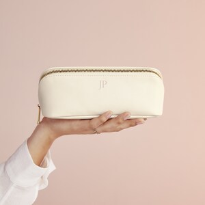 May include: A white leather cosmetic bag with a gold zipper and the initials "JP" embossed on the front.
