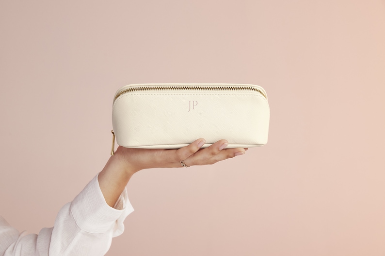 May include: A white leather cosmetic bag with a gold zipper and the initials "JP" embossed on the front.
