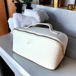 May include: White leather cosmetic bag with a gold zipper and handle. The bag has the initials "JP" embossed in gold on the front.