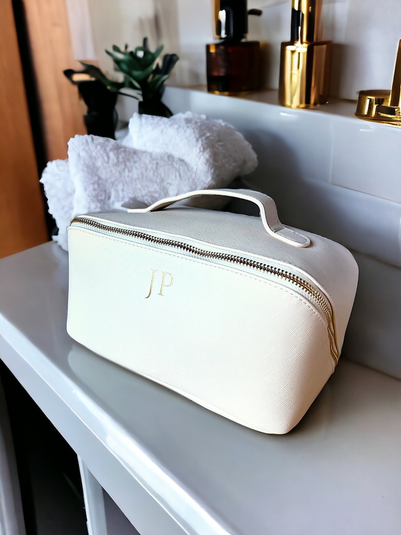 May include: White leather cosmetic bag with a gold zipper and handle. The bag has the initials "JP" embossed in gold on the front.