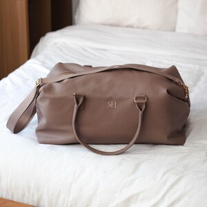 May include: A brown leather travel bag with a top handle and a shoulder strap. The bag has a zipper closure and is monogrammed with the initials "SH".
