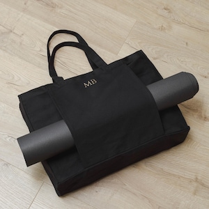 May include: Black canvas tote bag with a separate pocket for a yoga mat. The bag has the initials "MB" embroidered on the front.
