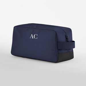May include: A navy blue wash bag with a black base and a white monogram "AC" on the front.