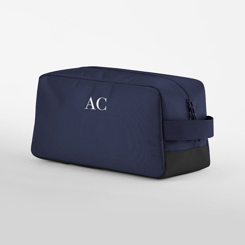 May include: A navy blue wash bag with a black base and a white monogram "AC" on the front.