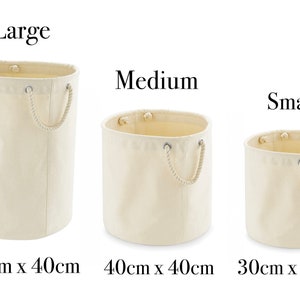 May include: Three cylindrical off-white canvas storage baskets with rope handles. The large basket is 60cm x 40cm, the medium basket is 40cm x 40cm, and the small basket is 30cm x 30cm. Each basket features metal grommets for the rope handles.