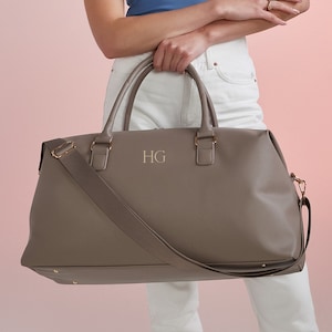 May include: A gray leather travel bag with a shoulder strap and gold hardware. The bag has the initials "HG" embossed on the front.