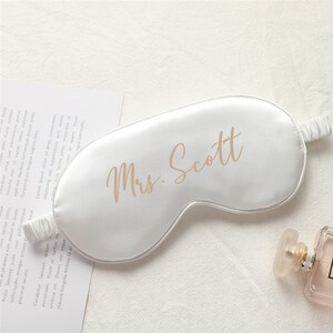 以下が含まれることがあります： ゴールドの文字で「Mrs. Scott」と書かれた白いサテン製のアイマスクです。
