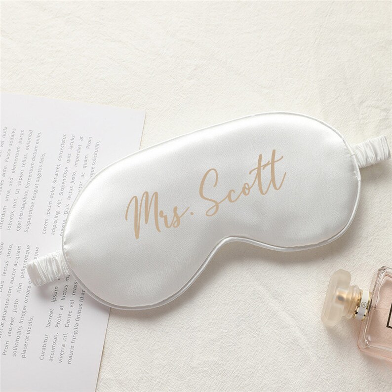 以下が含まれることがあります： ゴールドの文字で「Mrs. Scott」と書かれた白いサテン製のアイマスクです。