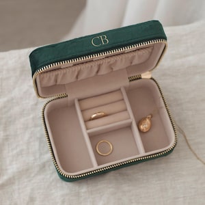 May include: A green velvet jewellery box with a gold zipper and the initials "CB" on the top. The box is open and has compartments for rings and a necklace.