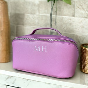 May include: A lavender-colored cosmetic bag with a zipper closure and a silver handle. The bag has the initials "MH" embroidered on the front in white.