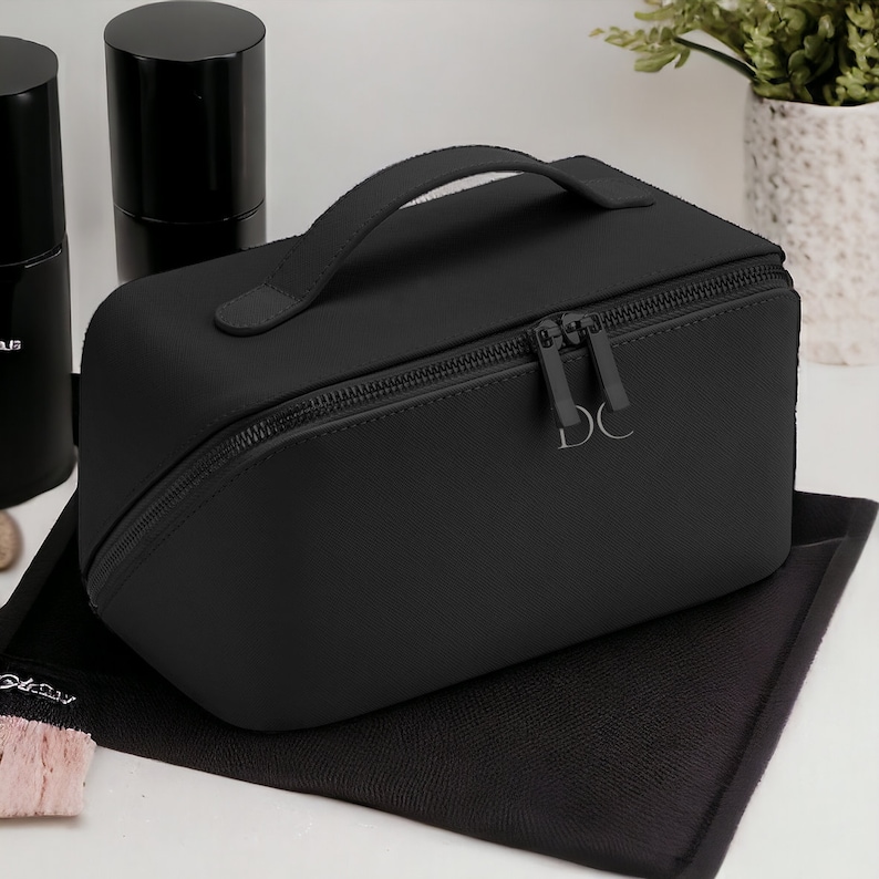 May include: Black zippered travel case with a top handle and the initials "DC" embossed on the front.