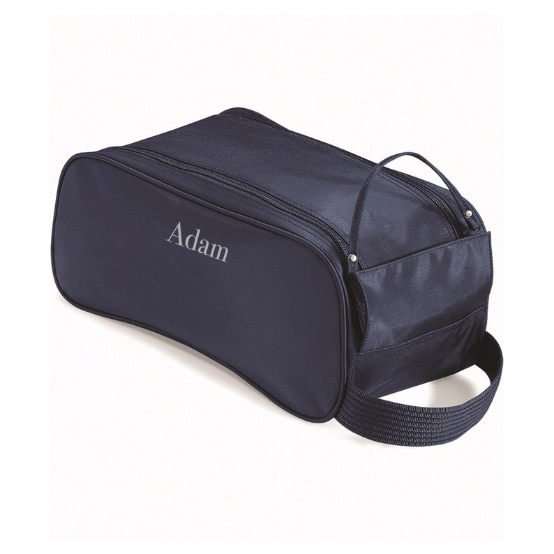 Puede incluir: Una bolsa para zapatos de color azul marino con cierre de cremallera y asa. La bolsa tiene un peque&ntilde;o bolsillo lateral y el nombre "Adam" est&aacute; bordado en la parte delantera.