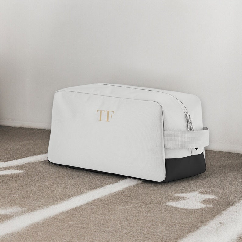 May include: White travel bag with a black base and a zip fastening. The bag has a black strap and the initials "TF" embroidered on the front.
