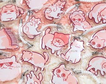 May include: A collection of clear acrylic charms featuring various illustrated cats in shades of pink and white. Each charm includes a white cord loop for hanging and the text SHIROUU_KUN printed on the surface of the cat designs.