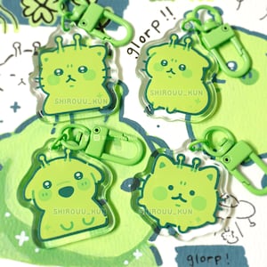Puede incluir: Cuatro llaveros de acrílico transparente con criaturas de dibujos animados de color verde lima con antenas y el texto SHIROUU_KUN. Cada llavero tiene un cierre de mosquetón de plástico verde lima a juego. Incluye tres figuras felinas.