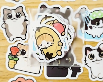 May include: A sheet of stickers featuring cute cartoon cats in various poses. The stickers are in a clear plastic bag. Some of the cats are wearing banana costumes, others are holding flowers, and some are wearing shower caps.