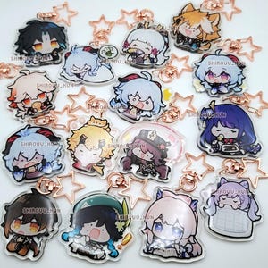 Puede incluir: Una colecci&oacute;n de llaveros de acr&iacute;lico transparente con varios personajes de anime estilo chibi con atuendos y expresiones coloridas. Cada dije est&aacute; unido a un broche de metal en forma de estrella de color oro rosa. El texto SHIROUU_KUN est&aacute; impreso.