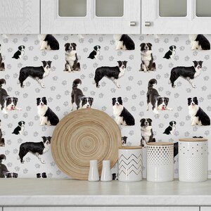 May include: A white kitchen countertop with a gray and white wallpaper featuring a repeating pattern of black and white border collie dogs and paw prints. There are three white ceramic canisters with different patterns on the counter.
