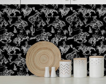 May include: Black and white kitchen backsplash with a repeating pattern of cowboys riding horses and cacti. The backsplash is behind a counter with four white ceramic canisters and a wooden plate.