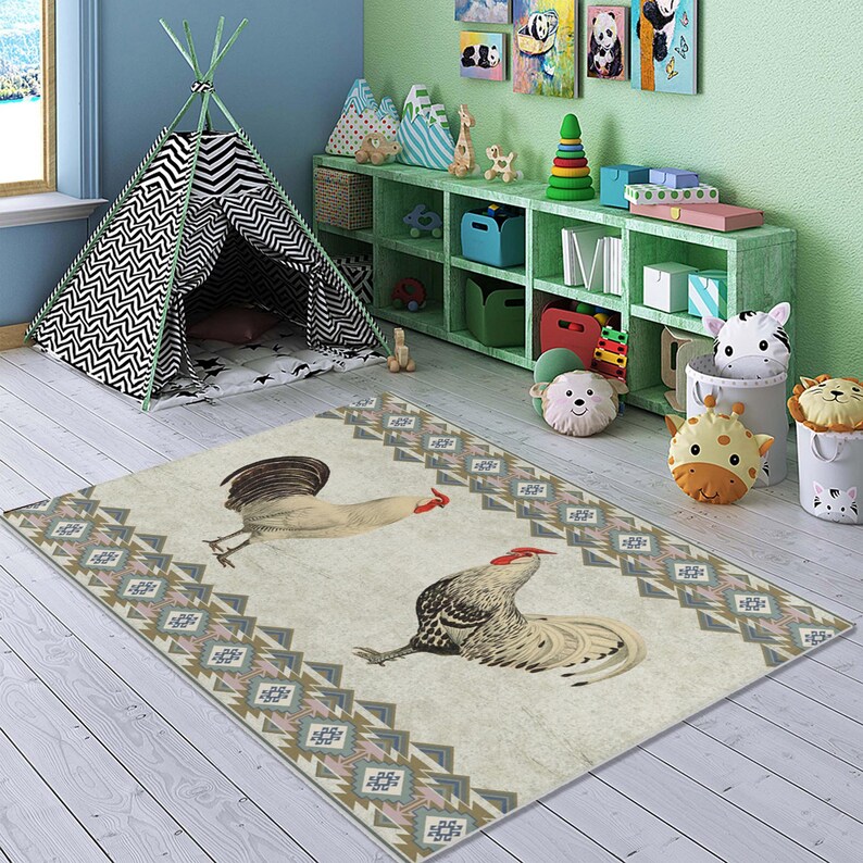 May include: A cream-colored rug with a geometric pattern in shades of brown, blue, and pink. Two roosters are featured on the rug, one facing left and one facing right. The rug is on a wooden floor in a room with a teepee and a bookshelf.