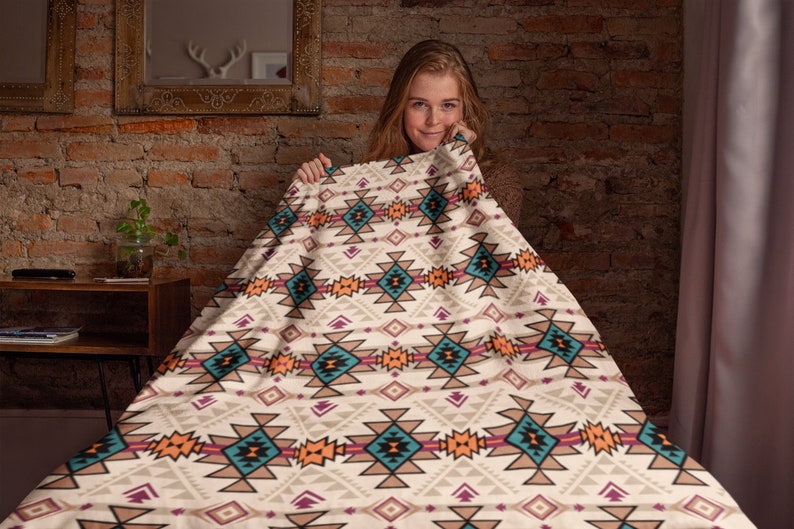 K&ouml;nnte beinhalten: Eine wei&szlig;e Decke mit einem geometrischen Muster in Orange-, T&uuml;rkis-, Braun- und Rosat&ouml;nen. Die Decke hat ein s&uuml;dwestliches oder indianisches Design.