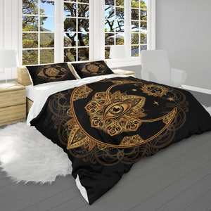May include: Black and gold duvet cover with a mandala design featuring an eye, moon, and sun. The duvet cover is on a bed with white pillows.