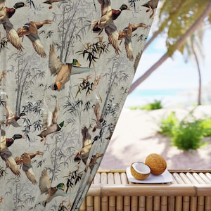 May include: A curtain with a repeating pattern of flying ducks and bamboo stalks in shades of brown, green, and gray. The curtain is hanging in front of a tropical beach scene with coconuts on a bamboo table.