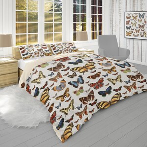 May include: A white duvet cover with a colorful butterfly pattern. The duvet cover features a variety of butterfly species in shades of blue, orange, yellow, and brown. The background is a cream color.
