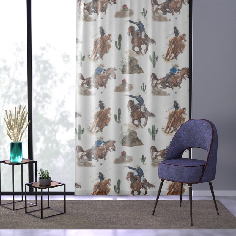 May include: White curtain panel featuring a repeating watercolor pattern of cowboys riding horses, cacti, and small rock formations. The curtain is hanging in front of a window, with a modern chair and side tables in the room.