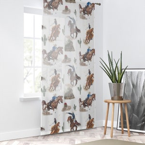 May include: Sheer white curtain panel featuring a repeating watercolor pattern of cowboys riding horses, cacti, and desert landscapes. The design includes cowboys in blue shirts and brown horses in action poses. The curtain is hanging in front of a window.