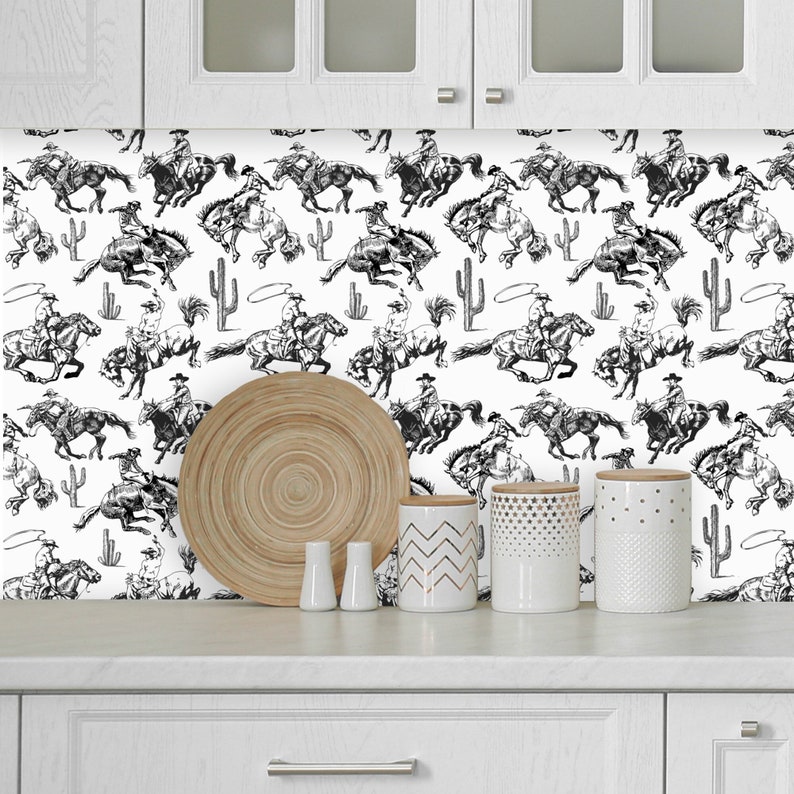 May include: Black and white wallpaper featuring a repeating pattern of cowboys riding horses. The cowboys are wearing hats and are holding reins. The horses are galloping and have flowing manes. The background is white with a cactus and lasso design.