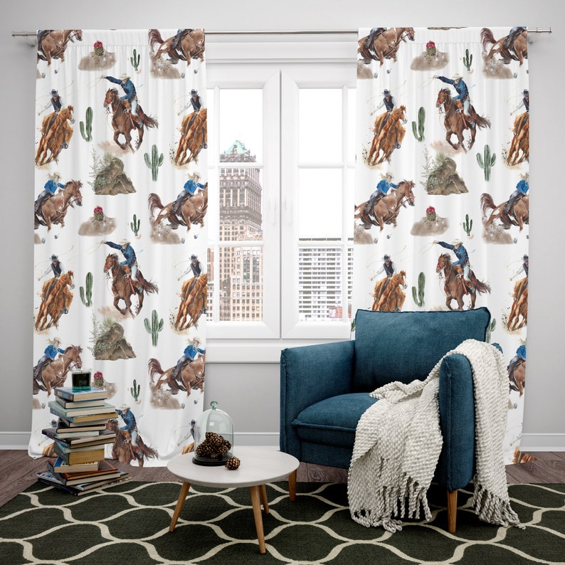 May include: White curtain panels with a repeating watercolor pattern of a rodeo scene. The design features cowboys on horseback, cacti, and desert plants. The curtains are hanging in front of a window, with a blue armchair and a small table in the foreground.