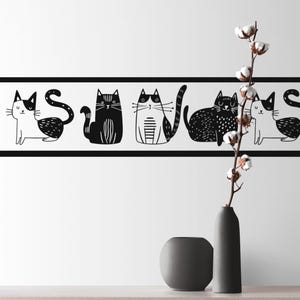 May include: A black and white cat border design on a white wall. The border features stylized cat illustrations in various poses. A gray vase holds a cotton branch, and a smaller gray vase sits nearby.