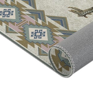 May include: Close-up of the edge of a rug with a geometric pattern in shades of brown, blue, green, and pink. The rug has a gray backing with white stitching.