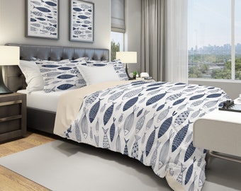 May include: A white and blue duvet cover with a pattern of stylized fish. The duvet cover is on a bed with white and blue patterned pillowcases. The bed is in a bedroom with a window and a nightstand.