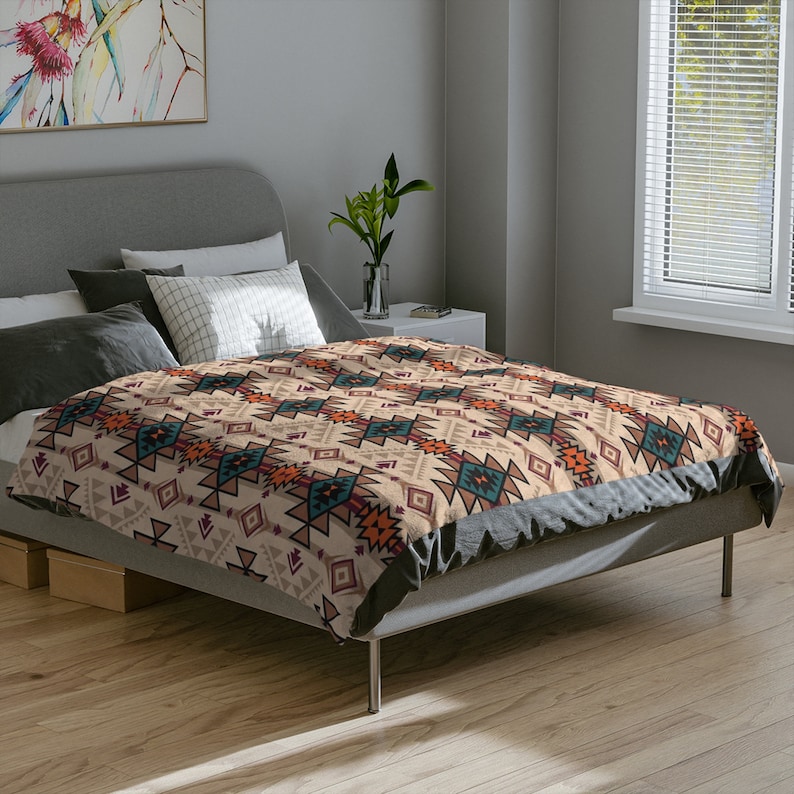 K&ouml;nnte beinhalten: Ein Bett mit einem grauen Kopfteil und einem beigefarbenen Bettbezug mit einem geometrischen Muster in Orange-, Blau- und Braunt&ouml;nen. Der Bettbezug hat einen Fransenrand.