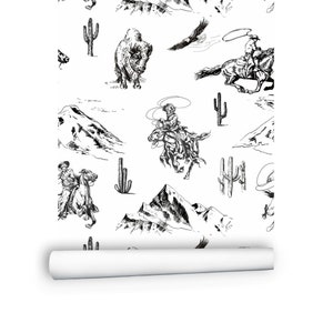 May include: White wallpaper roll featuring a black and white Western-themed pattern. The design includes illustrations of cowboys on horseback, mountains, cacti, bison, and eagles. The roll is partially unrolled, revealing the pattern.