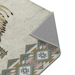 May include: A beige rug with a geometric pattern in shades of blue, green, and pink. The rug features a stylized bird design in the upper left corner. The rug has a gray backing with a stitched edge.