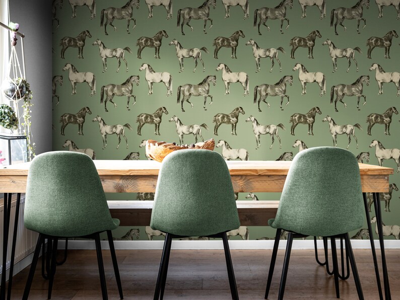 May include: A dining room with a green wallpaper featuring a repeating pattern of horses. The wallpaper has a vintage feel. There are three chairs with green upholstery and black metal legs. The chairs are arranged around a wooden table.