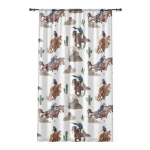 May include: White curtain with a repeating watercolor pattern of cowboys riding horses, cacti, and desert landscapes. The cowboys wear blue and black attire. The curtain is hung on a dark brown rod.