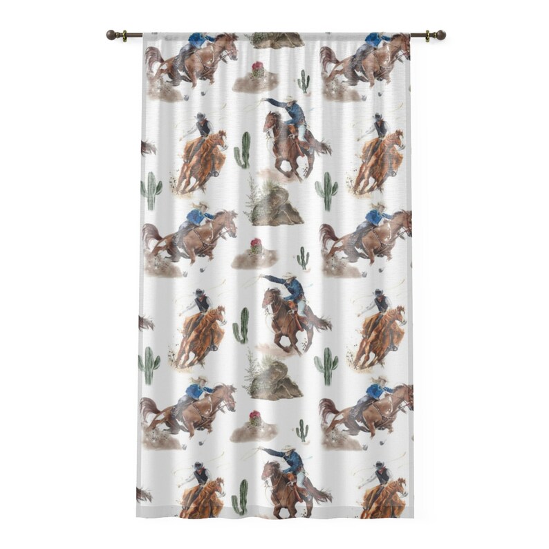 May include: White curtain with a repeating watercolor pattern of cowboys riding horses, cacti, and desert landscapes. The cowboys wear blue and black attire. The curtain is hung on a dark brown rod.