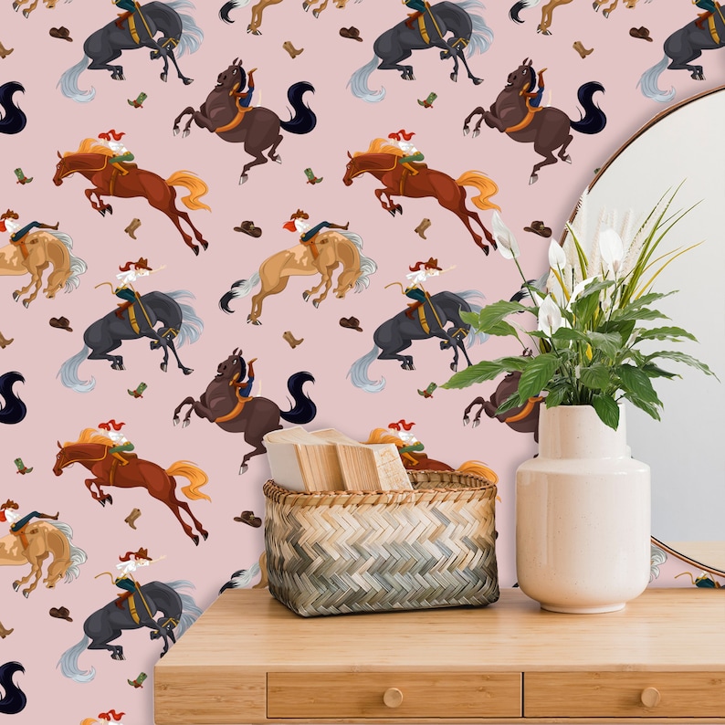 Peut inclure: Un papier peint rose avec un motif r&eacute;p&eacute;t&eacute; de cowboys &agrave; cheval. Les cowboys portent des tenues brunes et noires et les chevaux sont bruns, noirs et blancs. Le papier peint est agr&eacute;ment&eacute; d'un panier en osier, d'un vase de fleurs blanches et d'une table en bois.