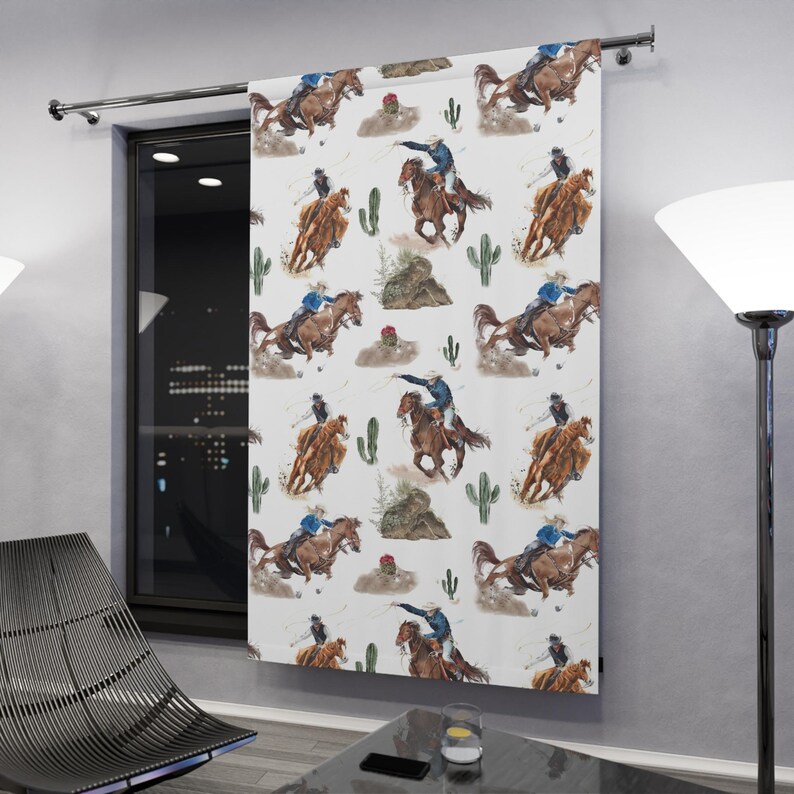 May include: White curtain panel featuring a repeating watercolor pattern of cowboys on horseback, cacti, and desert elements. The cowboys are depicted in blue and brown tones, with the horses in shades of brown. The design has a Western theme.