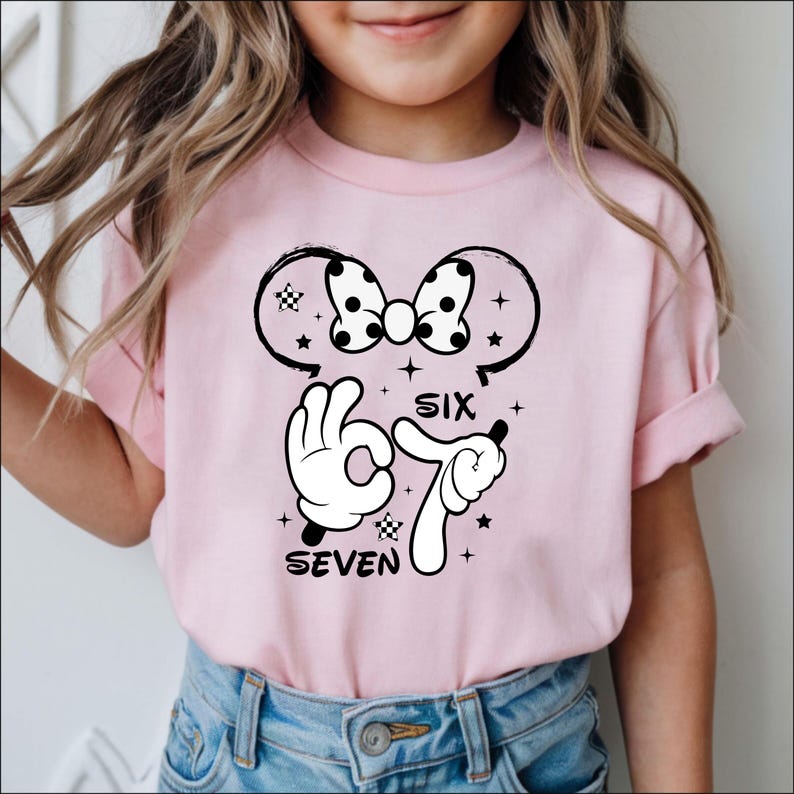 A young girl wearing a pink t-shirt with a cartoon character and text printed on it.