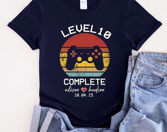 May include: Navy blue t-shirt with a retro-style video game controller graphic and the text "LEVEL 10 COMPLETE alison hudson 10.04.15".